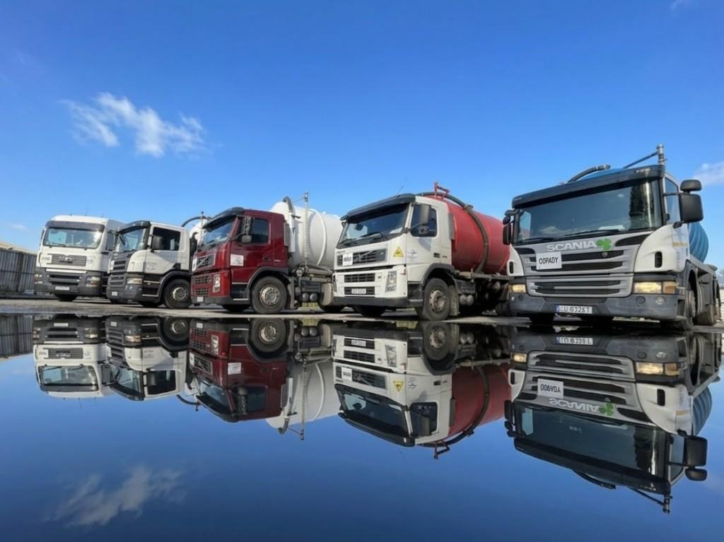 Flota wozów asenizacyjnych Szambo Lublin – szambiarki MAN, Scania i Volvo odbite w kałuży na placu w Lublinie